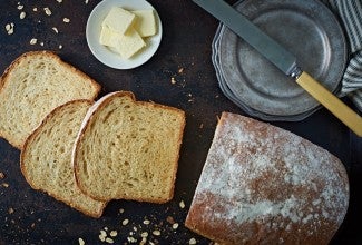 Loaf of oatmeal bread sliced, with knife and saucer of butter pats